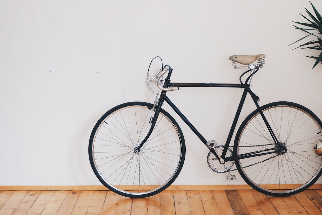 home-hero A vintage-style bicycle leaning against a clean white wall with wooden flooring, emphasizing minimalist design.